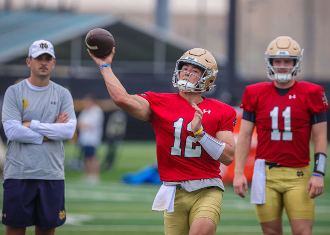 Tyler Buchner (12) throws a pass during a recent Notre Dame football practice as offensive coordinator Tommy Rees (left) and Ron Powlus III (11) look on.