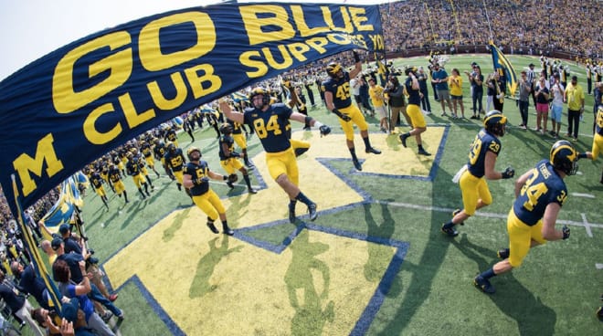 Michigan Wolverines football players run onto the field before a game and touch the banner.