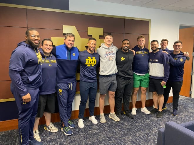 Cole Mullins, in gray, poses with head coach Marcus Freeman (left of Mullins), defensive coordinator Al Golden (left of Freeman), defensive line coach Al Washington (right of Mullins) and other members of the Notre Dame staff.
