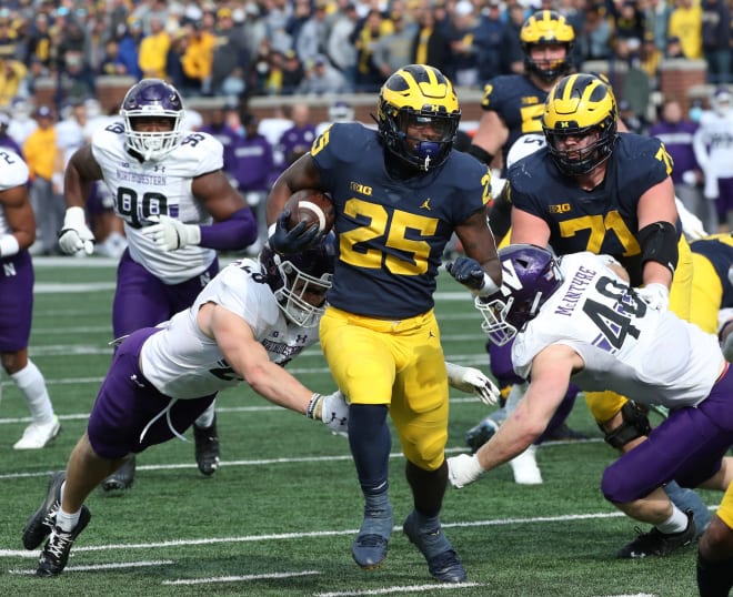 Michigan Wolverines running back Hassan Haskins (25) runs by Northwestern Wildcats defensive back Trent Carrington (20) and linebacker Peter McIntyre (40) during second half action Saturday.