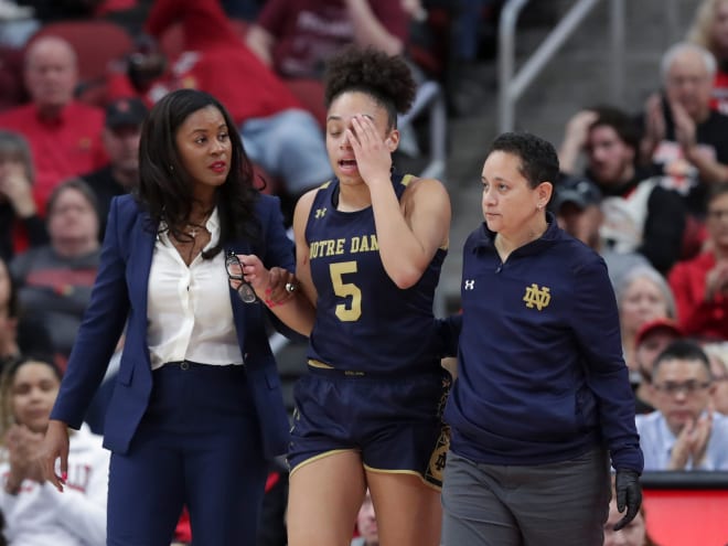 Notre Dame head coach Niele Ivey (left), and athletic trainer Anne Marquez (right) escort guard Olivia Miles off the court following a knee injury in the first half Sunday at Louisville.