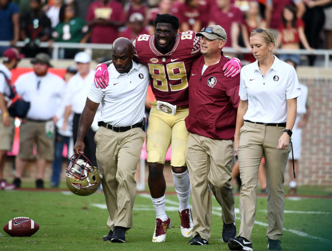 Longtime FSU athletic trainer Jake Pfeil (garnet jacket) helps receiver Keith Gavin off the field during a game in 2017.