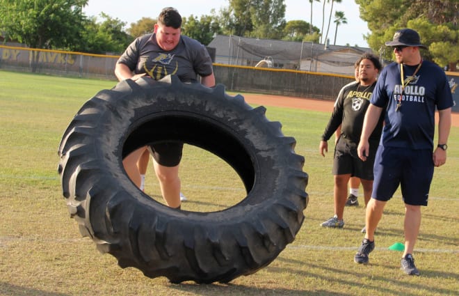Apollo offensive tackle Jacob Lee takes his turn in the tire flip with head coach Aaron Walls looking on.  The event was a relay with the tire traveling 15 yards for each player.