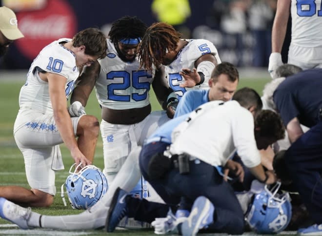 Tar Heels Drake Maye, Kaimon Rucker, and Jahvaree Ritzie pray for Tez Walker last Saturday night.