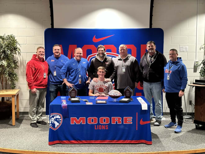 The Moore High football staff surrounds Evans at his signing ceremony