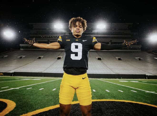 Seth Anderson poses at midfield at Kinnick Stadium during his visit in December 2022. The stadium is empty, and stadium lights illuminate the field in the night for the photo.